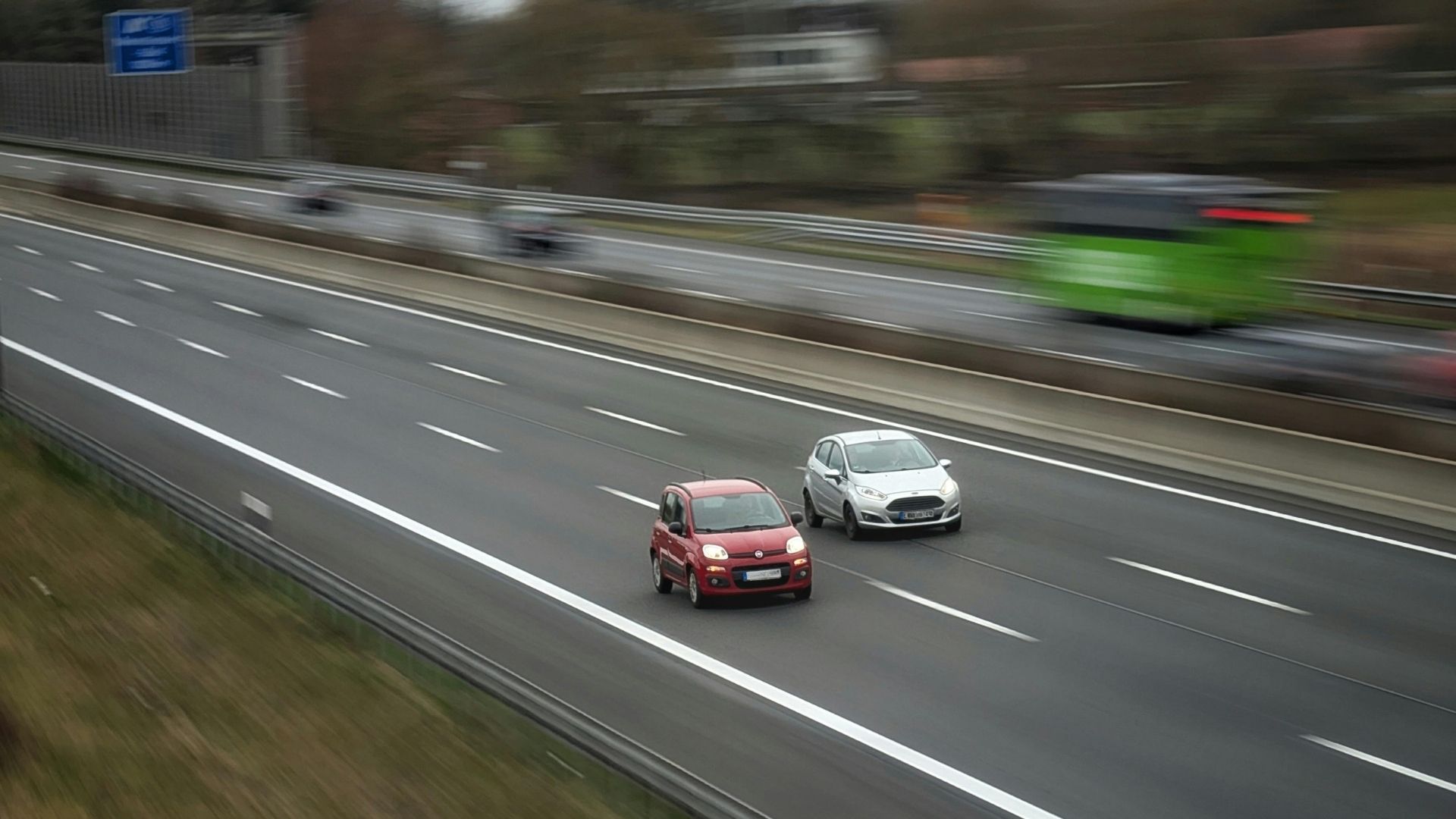 Un coche rojo y un coche gris en una autopista a gran velocidad.